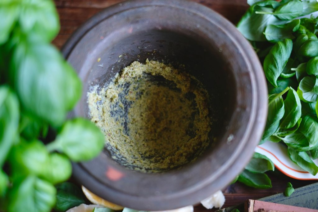 Grinding the pistachio and pine nuts, garlic, and salt for basil pesto in a pestle and mortar