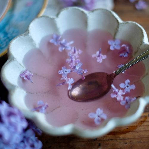 Simple Syrup in a bowl with a spoon and lilac blossoms